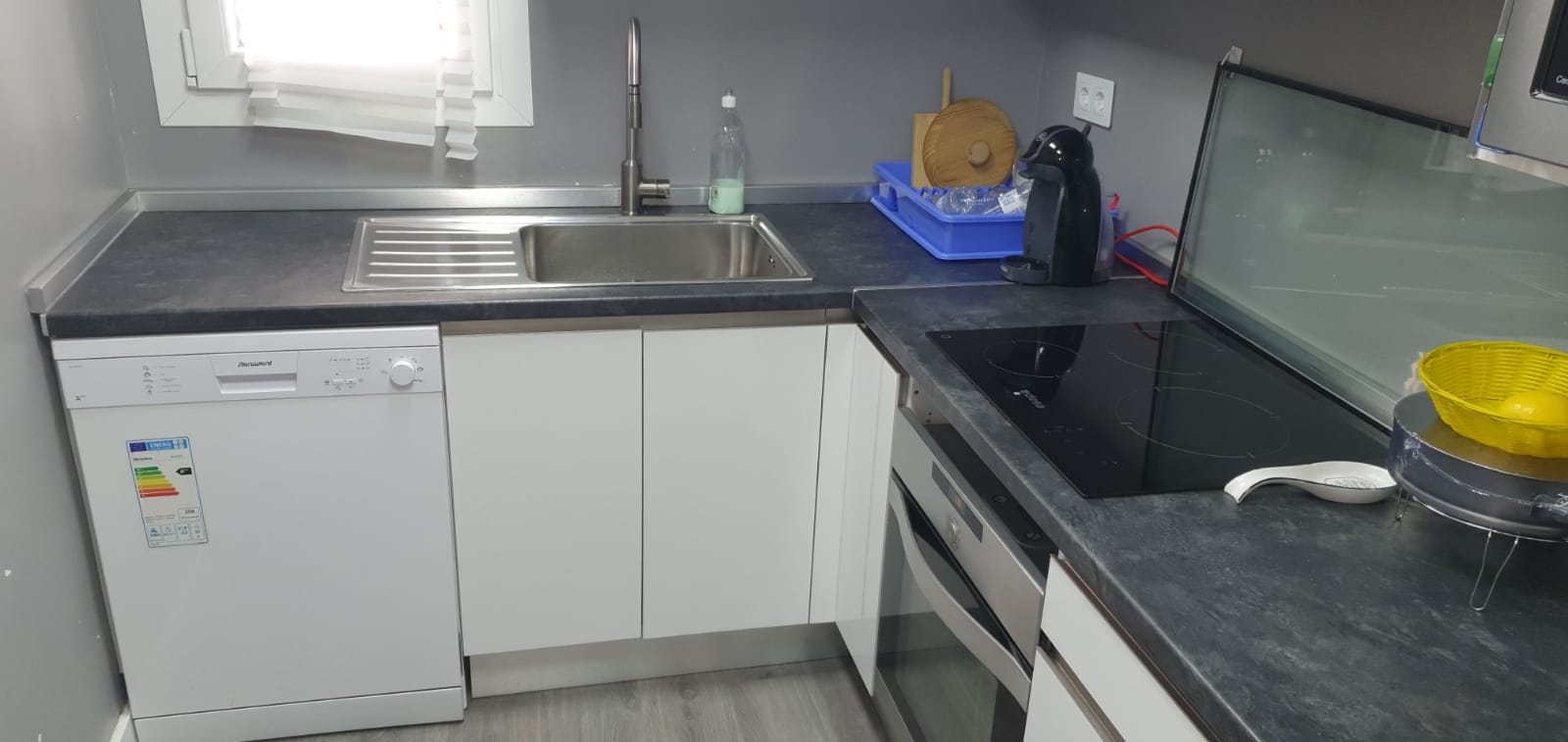 Cocina blanca reformada en Madrid con encimera oscura y fregadero bajo ventana