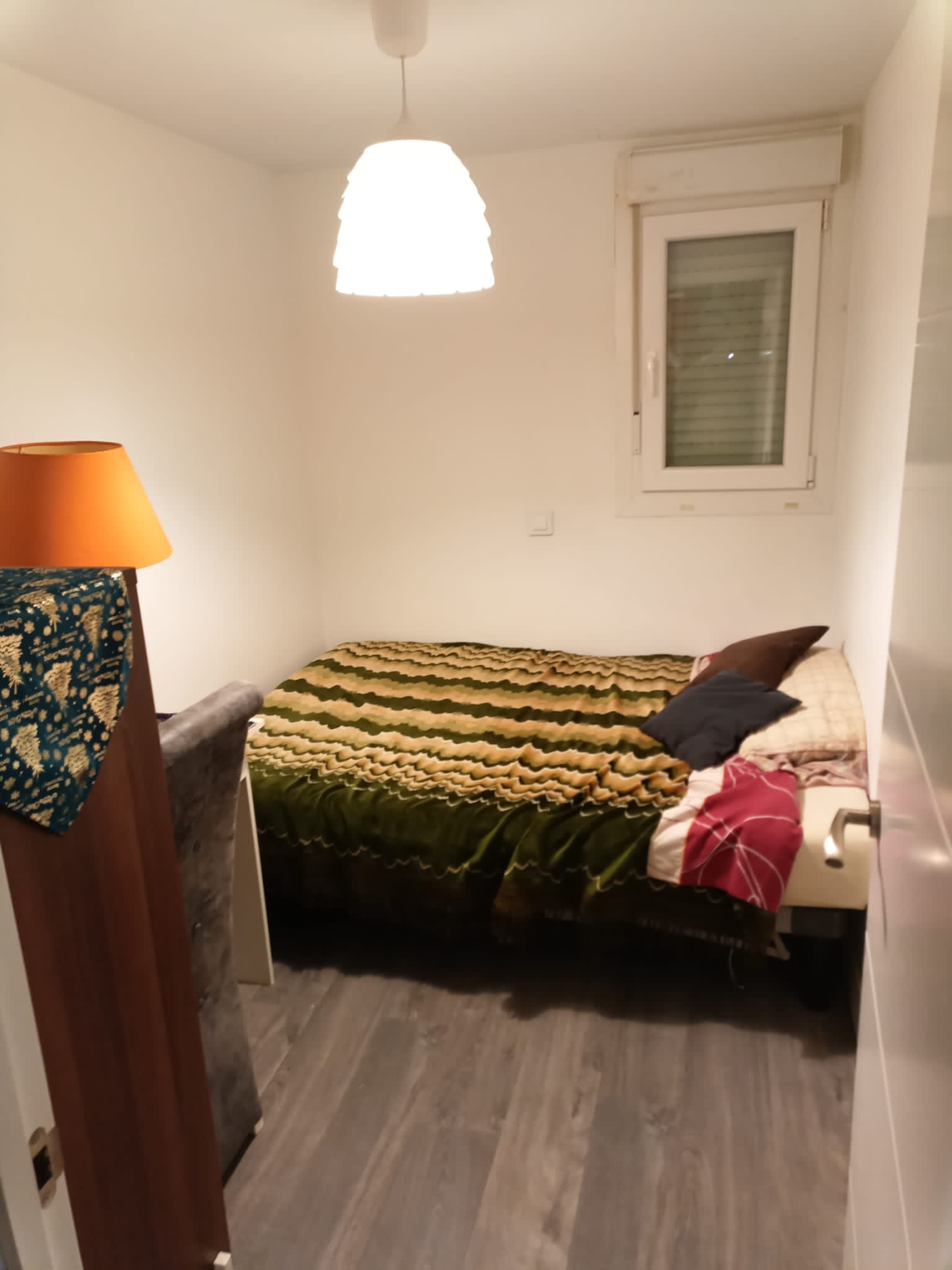Dormitorio estrecho reformado con lámpara colgante, cama y suelo gris