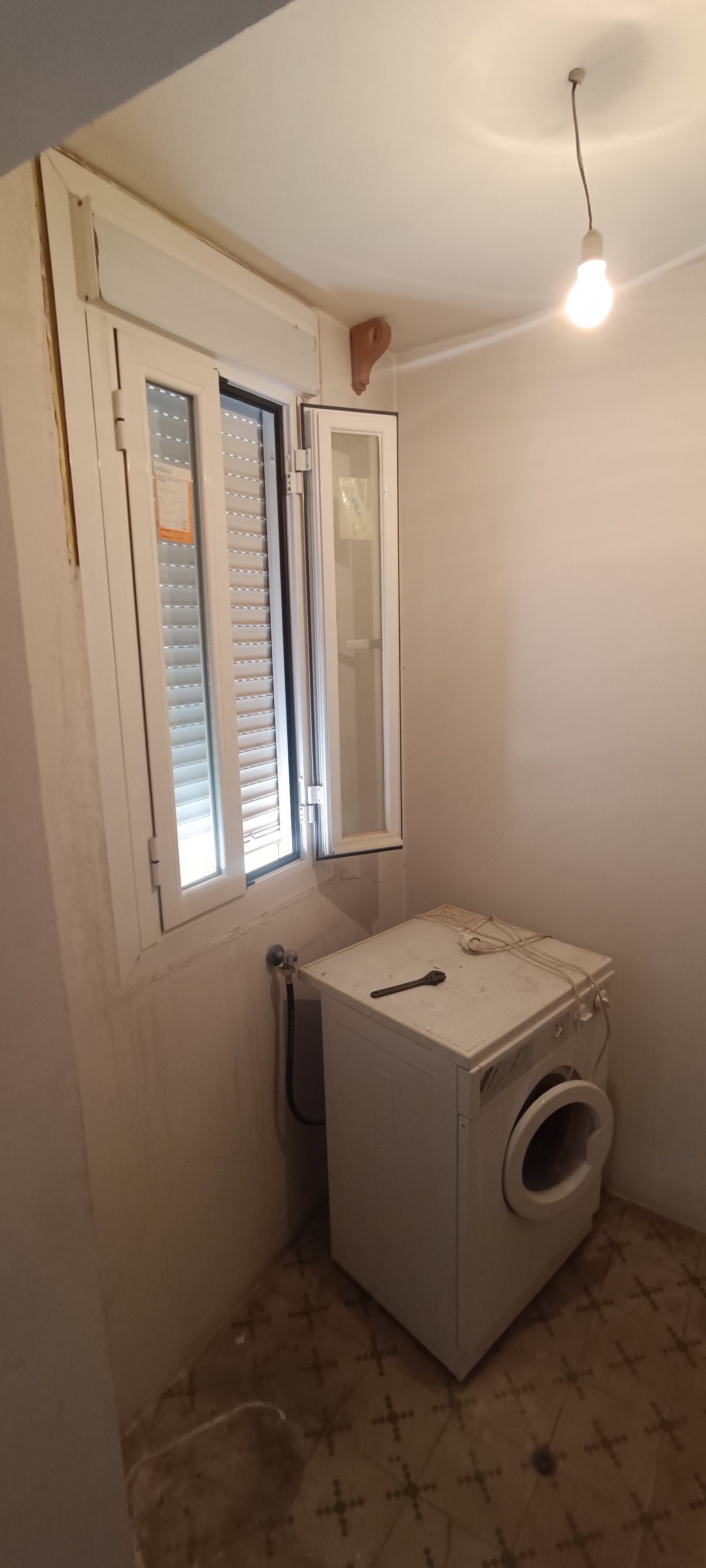 Cuarto estrecho con lavadora, ventana y pared beige antes de renovar