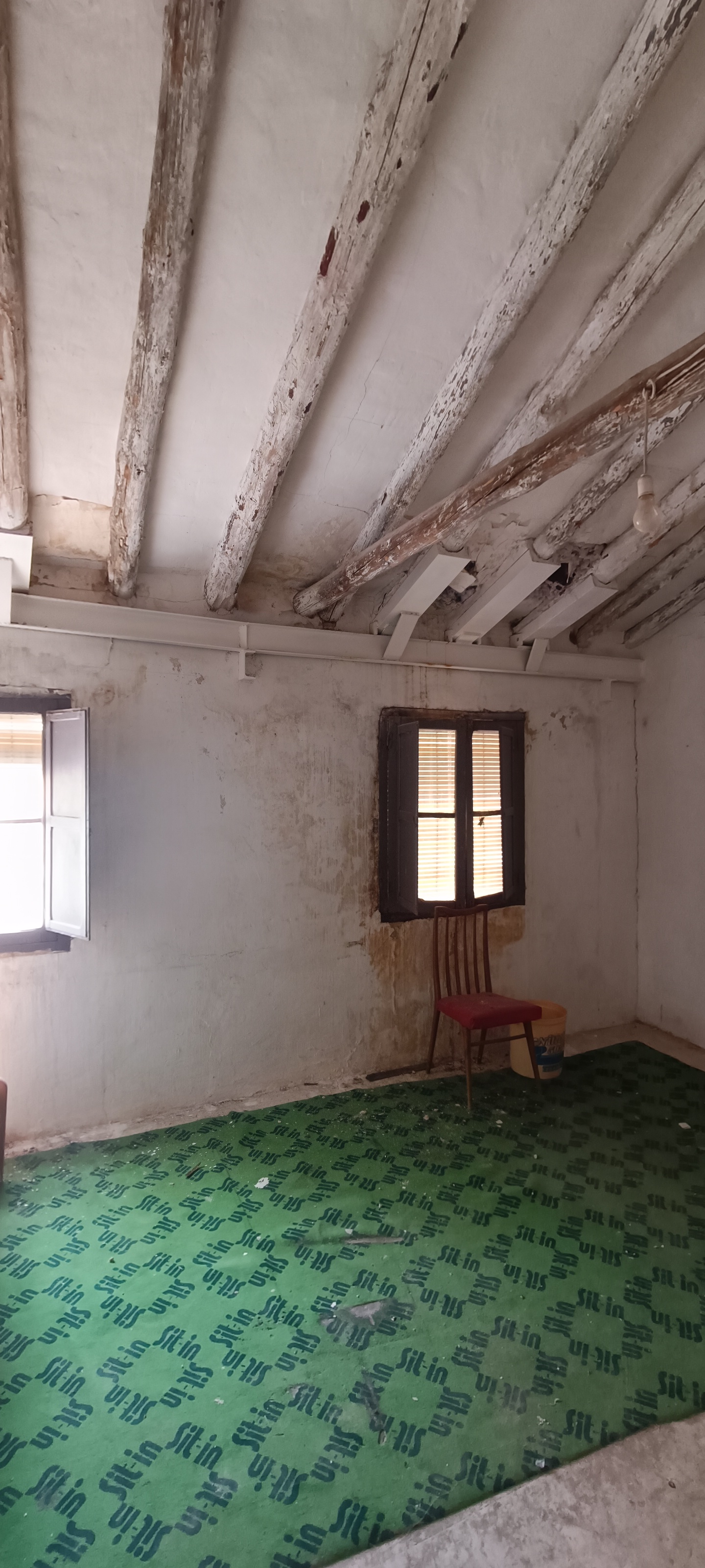 Salón antiguo con suelo verde, paredes sin terminar y vigas antes de rehabilitar