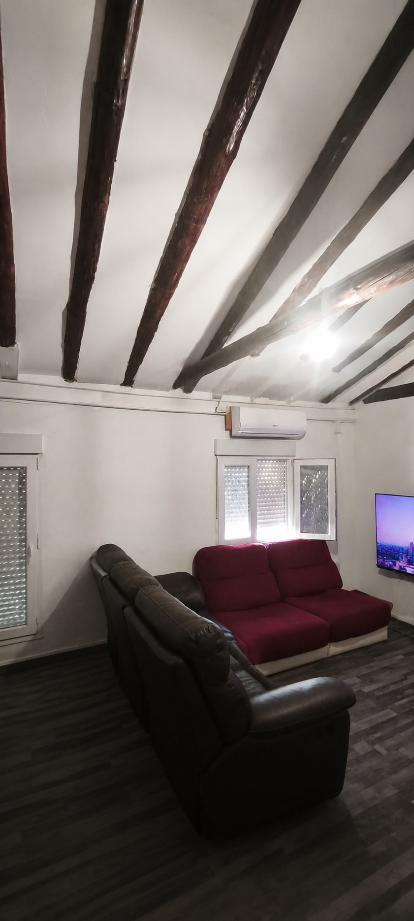 Salón rehabilitado con vigas restauradas, suelo oscuro y zona de estar