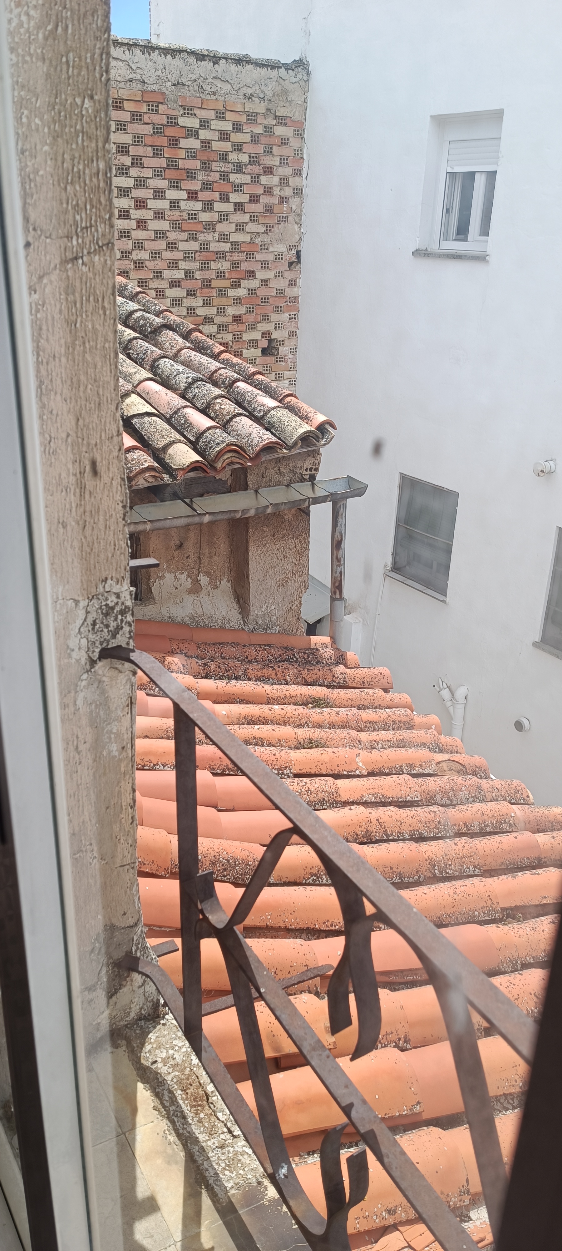 Vista exterior de tejado antiguo con tejas deterioradas junto a barandilla
